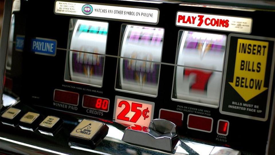 Walze eines Spielautomaten neben einer Sanduhr und einem Taschenrechner auf einem dunklen Holztisch