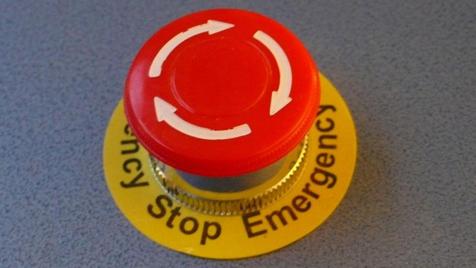 Roter Knopf auf einem Holztisch neben zugeklapptem Laptop und Casino-Chips als Symbol für den Panikknopf